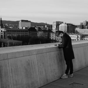 A person leans pensively on the Oslo Opera House rooftop overlooking the city skyline.