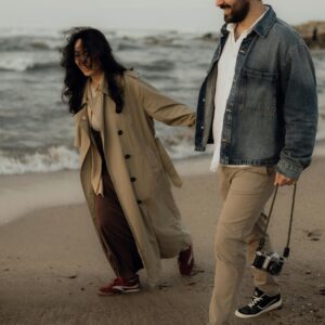 A joyful couple walking on a sandy beach holding an old camera.
